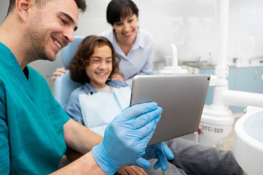 Dentist showing a tablet to a young patient and parent highlighting social media marketing for dentists