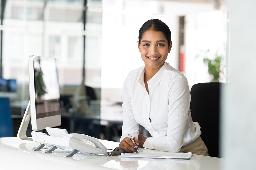 Portrait of beautiful young businesswoman sitting at her desk in front of computer and taking notes